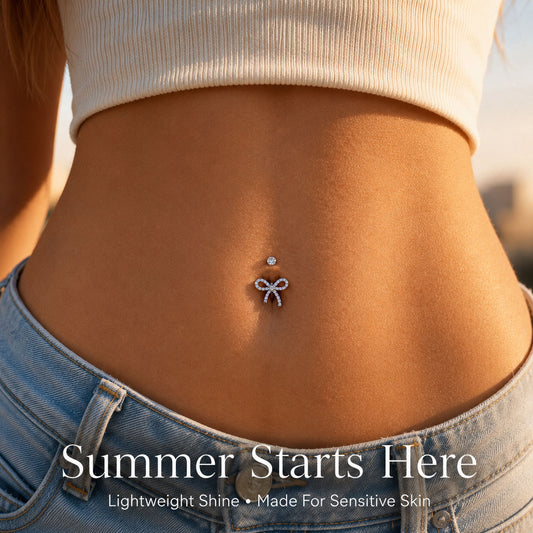 Young woman wearing Dazzling Titanium Bow Belly Button Ring, left tail shorter than right, on beach in white bikini, CZ sparkle visible