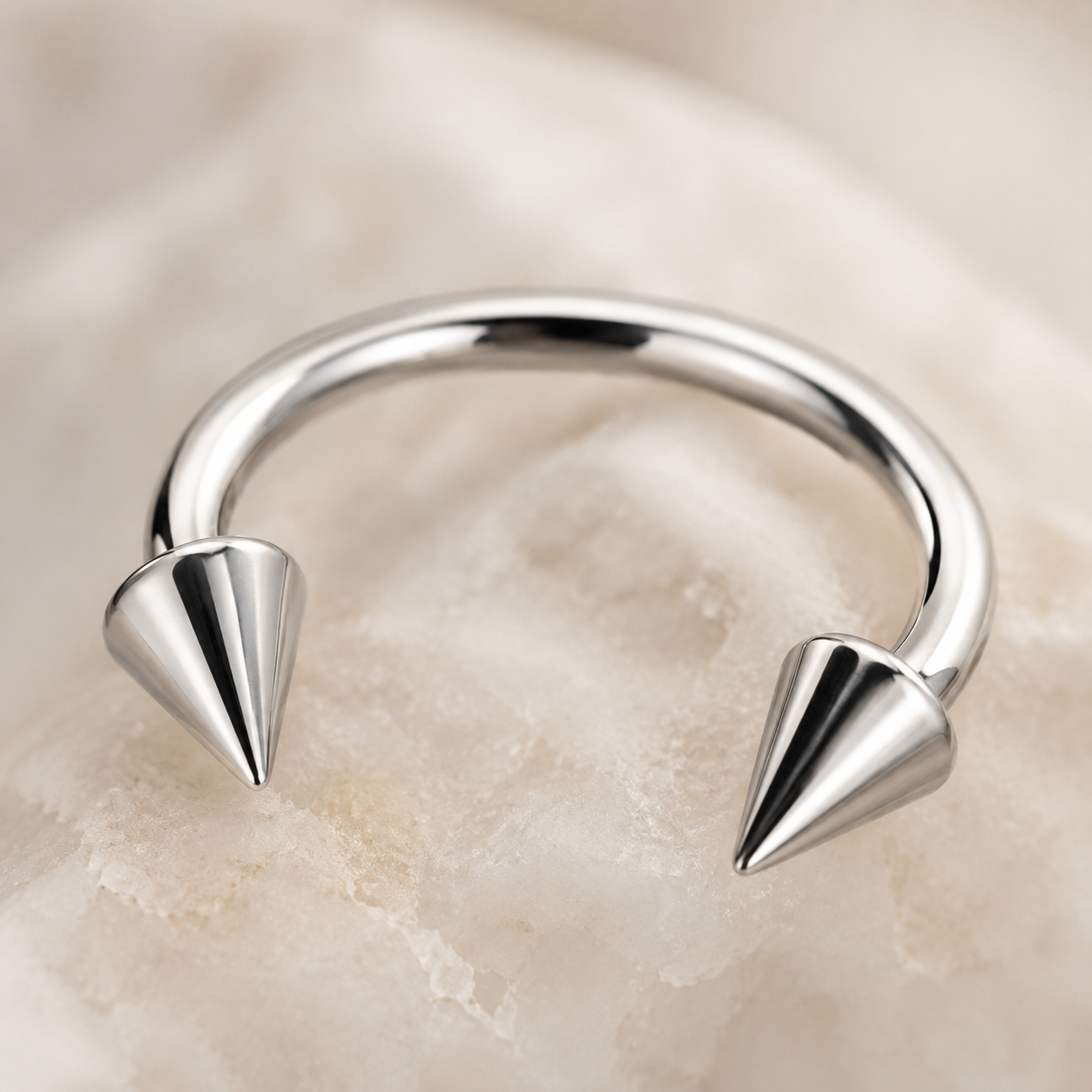 Macro detail of polished titanium horseshoe nose ring with cone spike ends and smooth curved bar