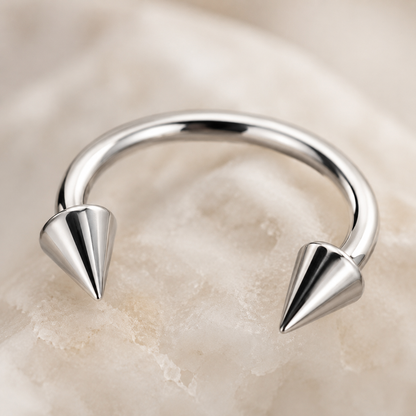Macro detail of polished titanium horseshoe nose ring with cone spike ends and smooth curved bar